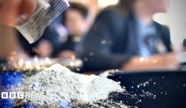 A pile of white powder has just been poured from small plastic bag on to a desk in a stylised image with young people in school uniform blurred in the background.