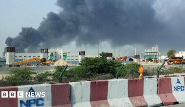 People run across a road with black smoke in the background.