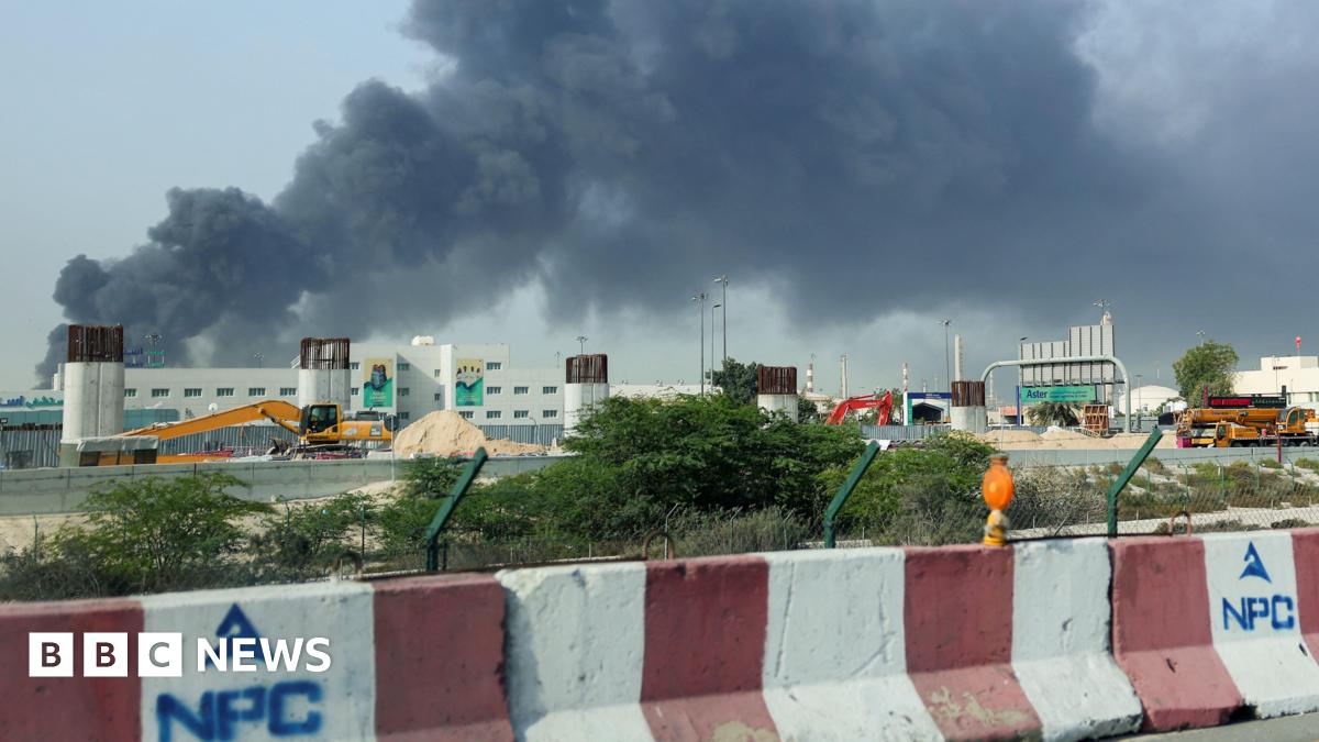People run across a road with black smoke in the background.