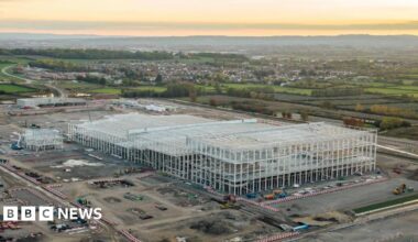 An artist's impression of the Somerset gigafactory building.  There are hedges  and a walkway. People are walking and some are on bikes.