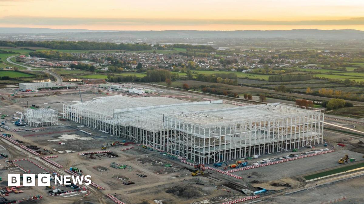 An artist's impression of the Somerset gigafactory building.  There are hedges  and a walkway. People are walking and some are on bikes.