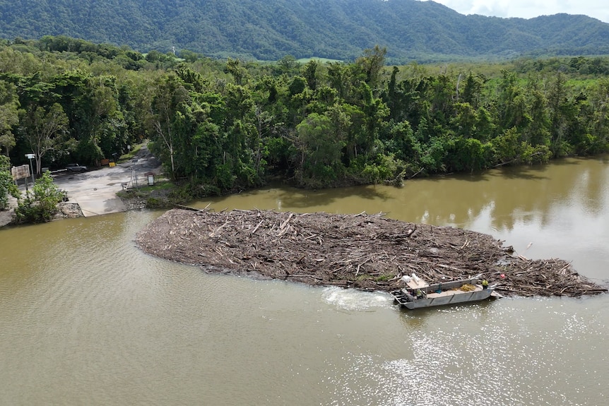 A pile of logs on a broad river, with a small boat close by. 