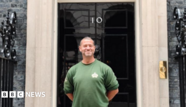 Smiling Karl Stevens, wearing a green gardening jumper, poses outside the door of No.10 Downing Street