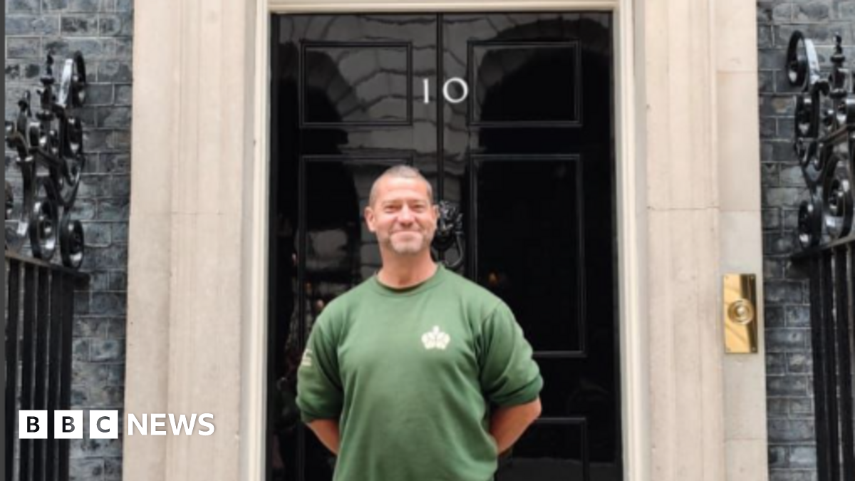 Smiling Karl Stevens, wearing a green gardening jumper, poses outside the door of No.10 Downing Street