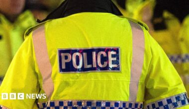 Generic image of a police officer in Greater Manchester, wearing a hi-vis yellow jacket with police labelled on the back.