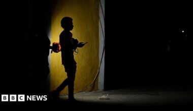 Two people holding a flashlight while walking on a dark street.