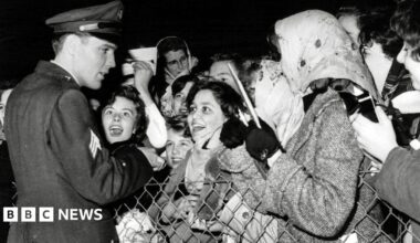Elvis greeting fans at  Prestwick Airport in 1960.  He is dressed in his military uniform. The fans are mostly female and looking at him with excitement and adoration.