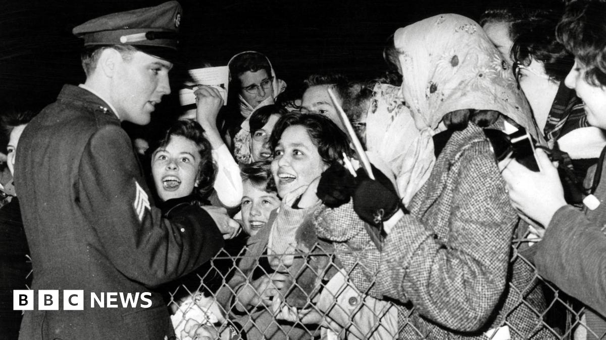 Elvis greeting fans at  Prestwick Airport in 1960.  He is dressed in his military uniform. The fans are mostly female and looking at him with excitement and adoration.