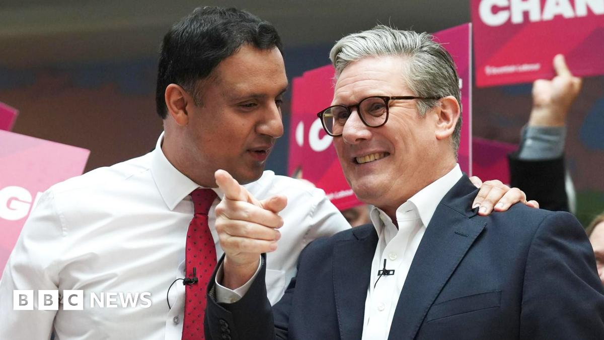 Anas Sarwar standing next to Sir Keir Starmer at a Labour Party event. Sarwar is wearing a white shirt and red tie and has his hand on the shoulder of Starmer, who is wearing a white shirt, a blue jacket and black-rimmed glasses.