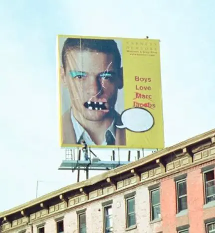 A large Banksy-altered billboard in New York City with a portrait of a man, an unfinished speech bubble, and the words "Boys Love Marc Jacobs".