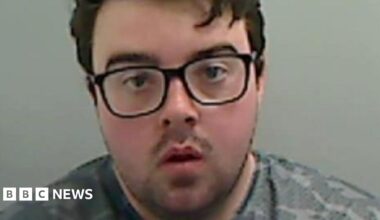 Mugshot of Callum Wray. He has a large round face, with black-framed glasses and short black hair.