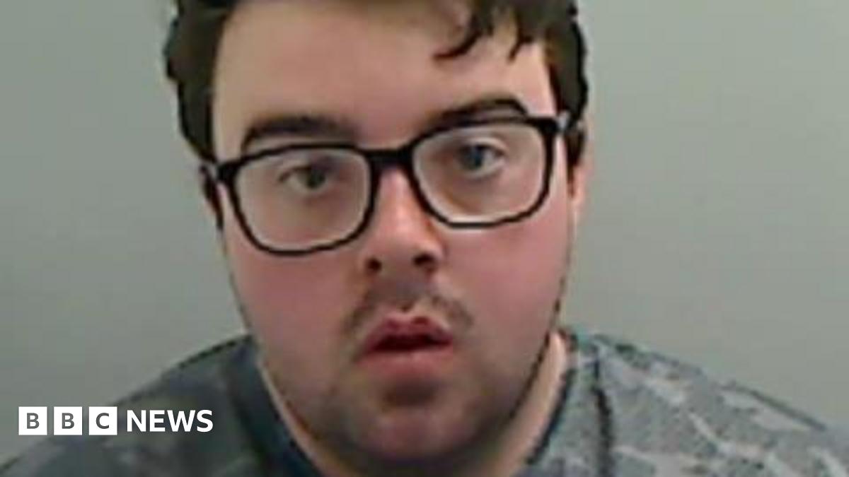 Mugshot of Callum Wray. He has a large round face, with black-framed glasses and short black hair.