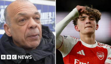 Jason Dozzell is wearing a dark coat standing outside the Ipswich Town football stadium. Max Dowman is on the pitch wearing a red Arsenal shirt.