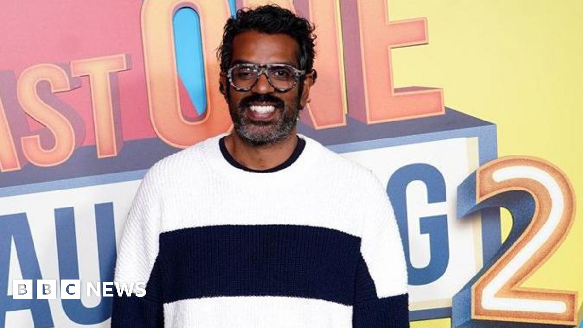 Romesh Ranganathan is seen during the photocall for Prime Video's Last One Laughing. He is wearing a black and white jumper and smiling and the logo for the programme is behind him.