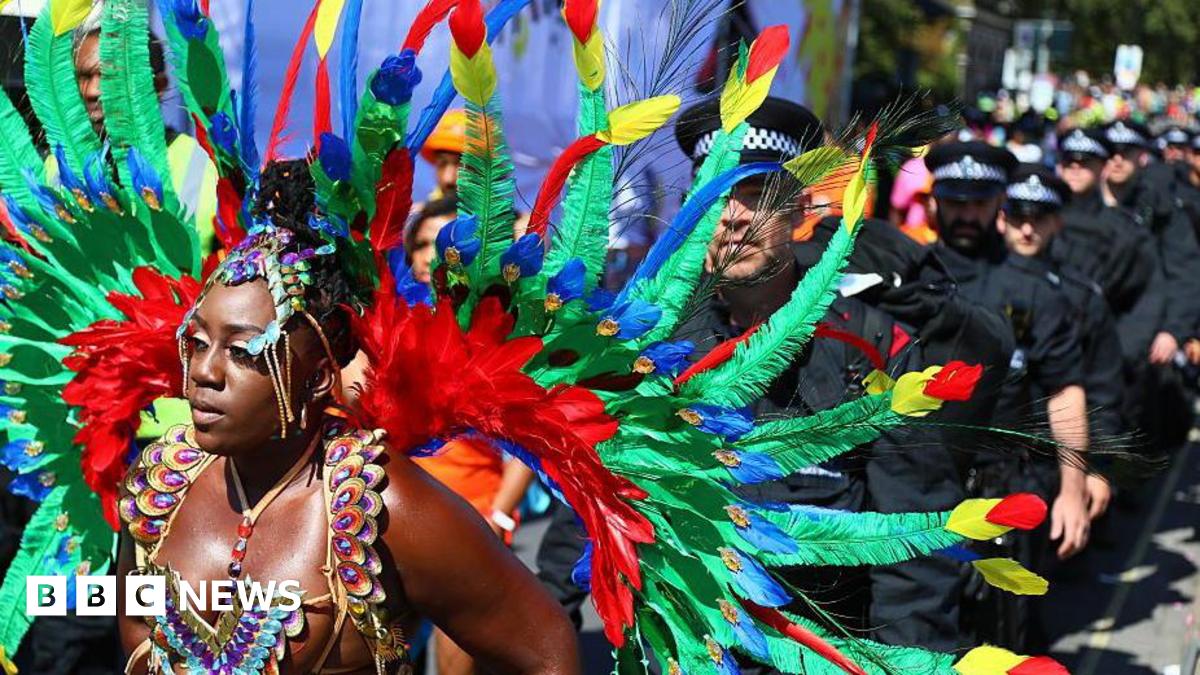 A brightly-feathered parade participant stands in front of a police line during the Notting Hill Carnival on August 25, 2025