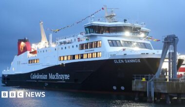 The MV Glen Sannox, a large black and white ferry with a red hull docked at a pier.