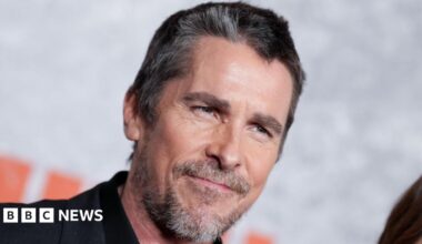 Headshot of Bale. He has greying black hair. He looks past the camera