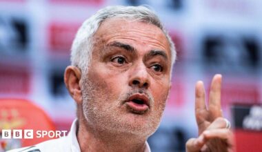 Close-up of Jose Mourinho speaking at a press conference. He has short grey hair, brushed to his right, and stubble. He is gesturing with his left hand.