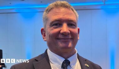 Derek Roberts is wearing a dark suit and a white shirt.