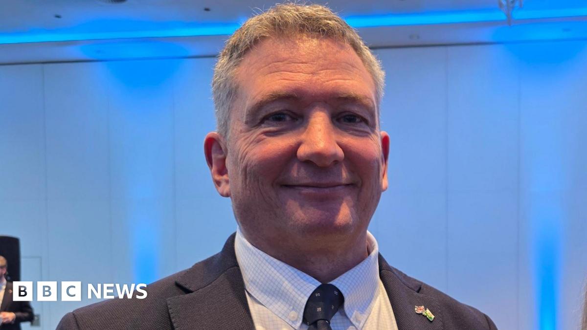 Derek Roberts is wearing a dark suit and a white shirt.