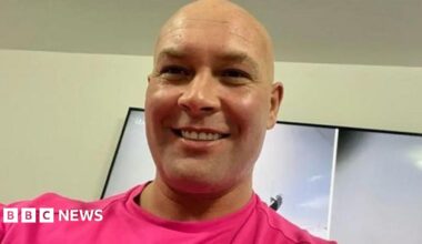 Head and shoulders image of Kirk Marsden, He is bald, smiling and wearing a bright pink tshirt