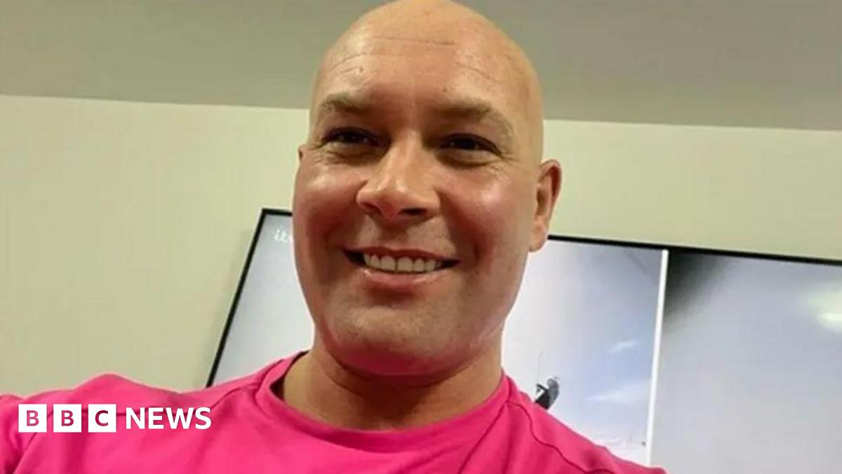 Head and shoulders image of Kirk Marsden, He is bald, smiling and wearing a bright pink tshirt