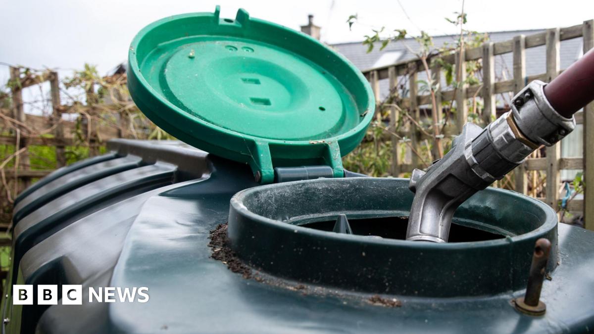A large plastic heating oil tank in a garden with its top open and a hose filling it.