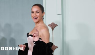 Meghan wears a light pink and black dress and poses in front of a light blue background, smiling.