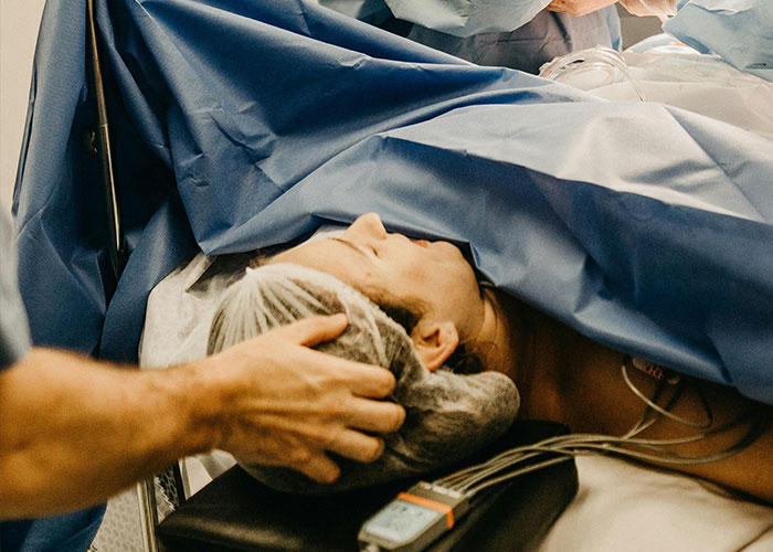 Patient lying on hospital bed covered in blue medical sheets with healthcare professional's hand on head, revealing medical secrets.