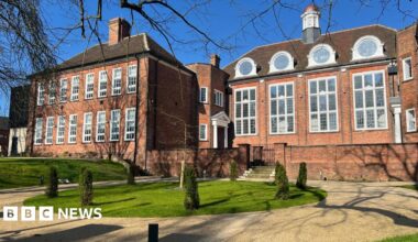 Large orange brick building with large rectangular white framed windows offset by courtyard