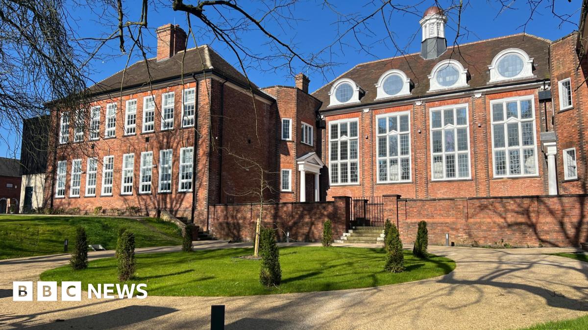 Large orange brick building with large rectangular white framed windows offset by courtyard