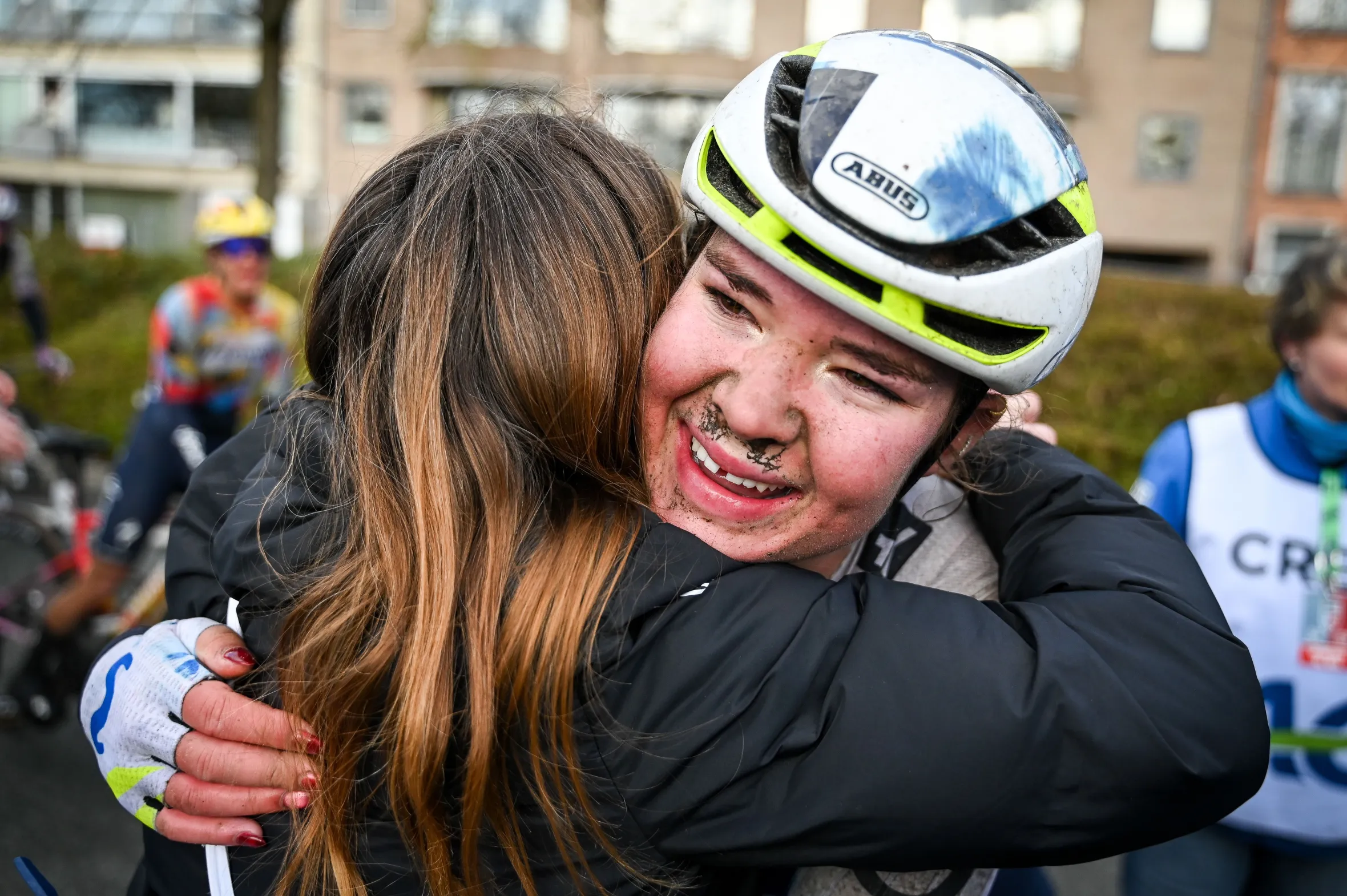 Carys Lloyd, covered in mud, smiles while hugging someone after the Ronde van Brugge cycling race.