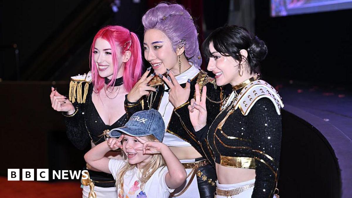 Cosplayers dressed as Huntr/x from Kpop Demon Hunters pose for a photo with a young girl