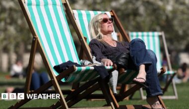 A woman sunbathes on a striped deck chair in a park