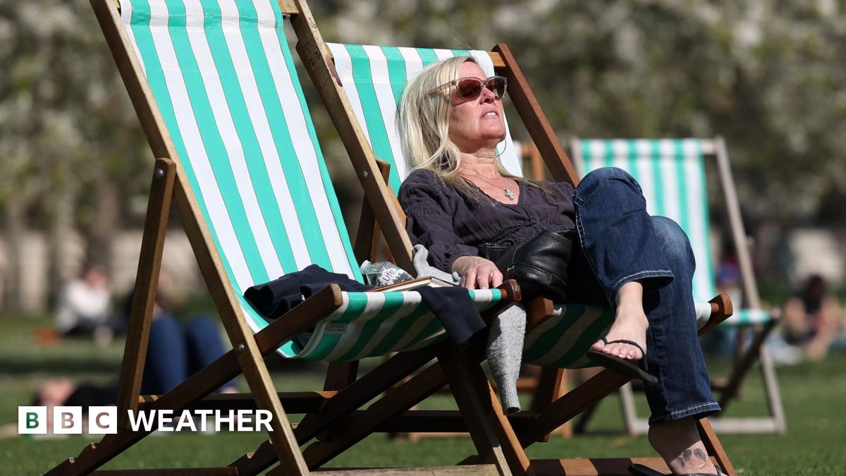 A woman sunbathes on a striped deck chair in a park