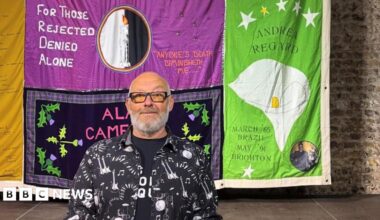 A woman with dark hair and a multiple colour jumper siting on a green sofa inside her living room.