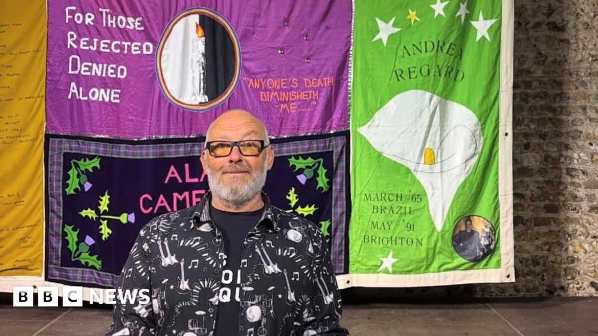 A woman with dark hair and a multiple colour jumper siting on a green sofa inside her living room.