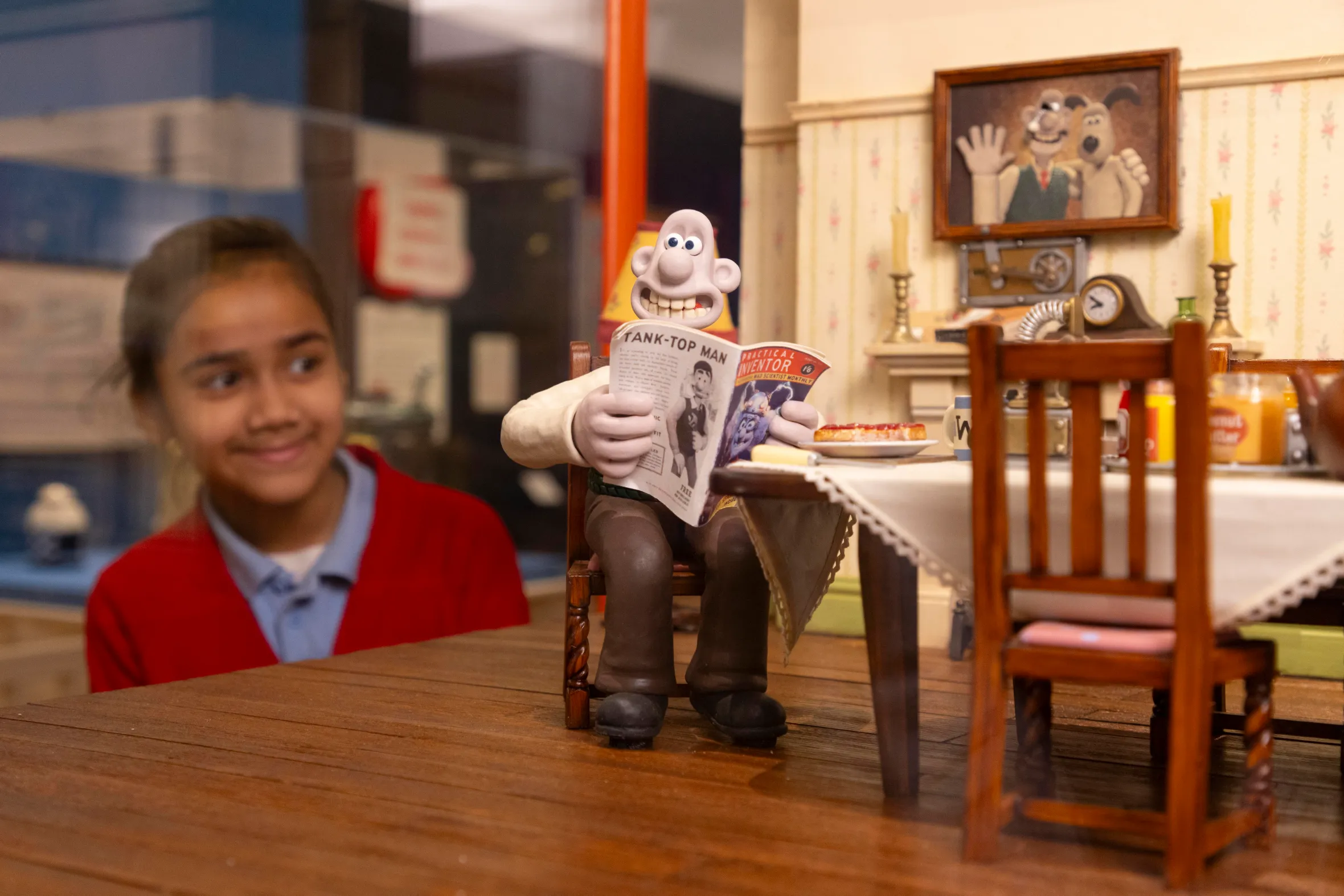 A child observes a Wallace & Gromit exhibit featuring Wallace reading a magazine.