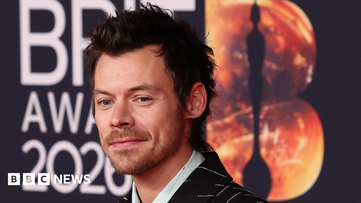A woman with dark hair and a multiple colour jumper siting on a green sofa inside her living room.