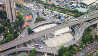 An ariel shot of the A40 showing small cars and London buses as well as surrounding houses and greenery.