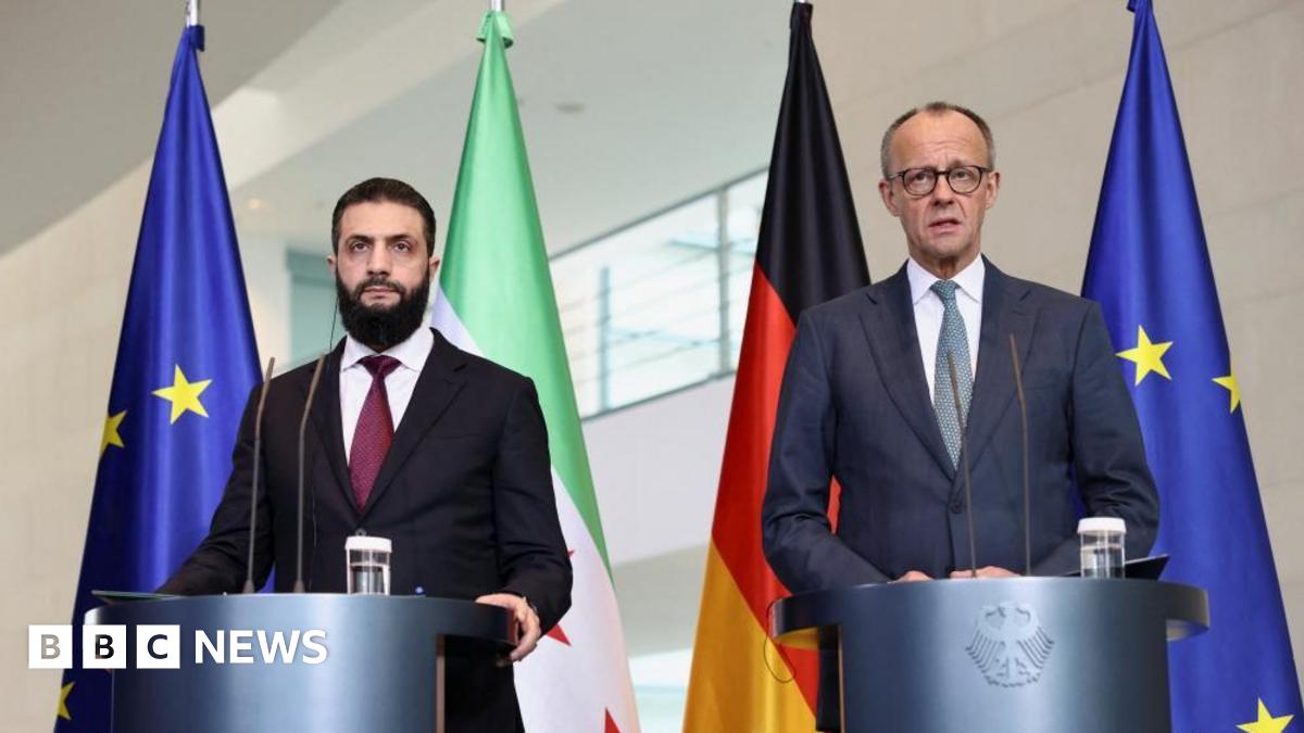 German Chancellor Friedrich Merz and Syrian President Ahmed al-Sharaa wearing suits and standing at podiums, in front of flags, hold a press conference at the Chancellery in Berlin, Germany