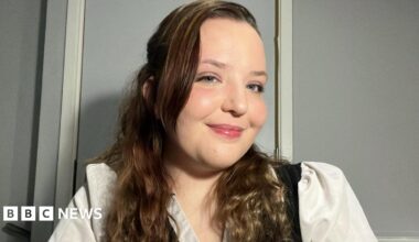 Aeryn Hill smiles at the camera and looks to the side. She has long wavy brown hair and is wearing white