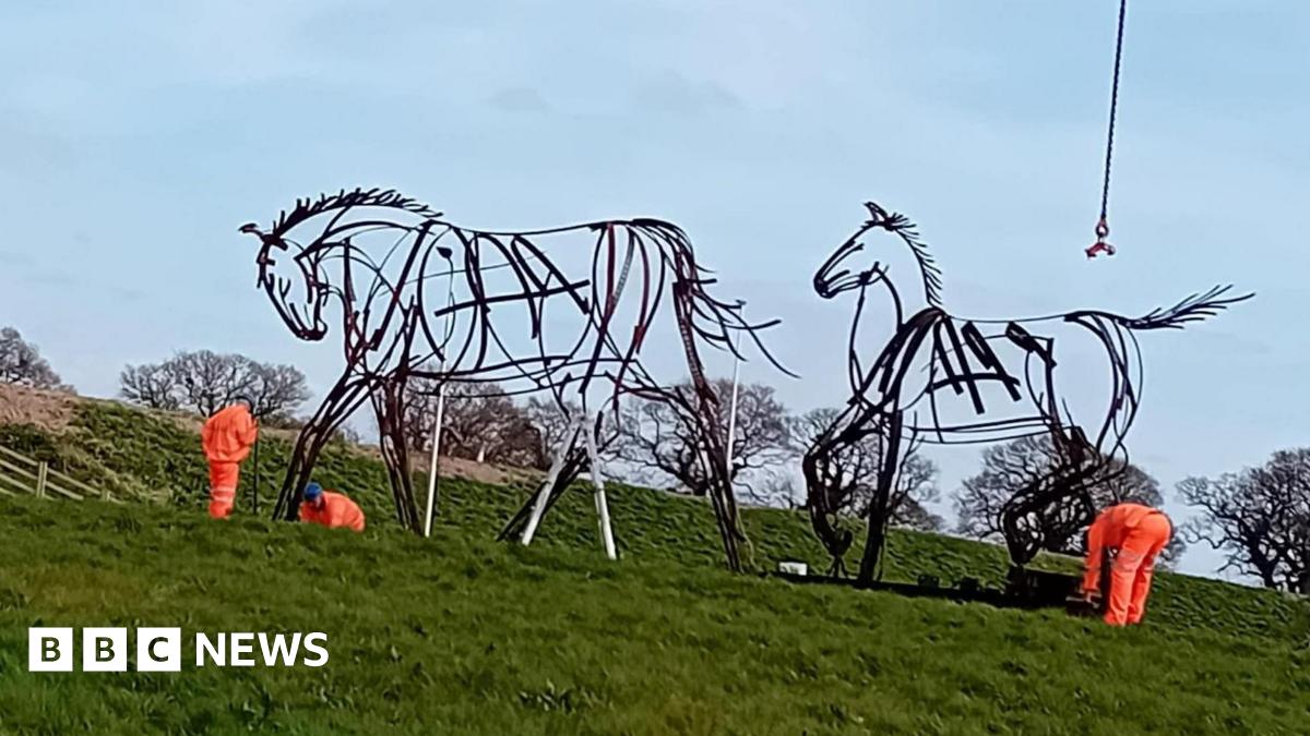 Three workman install two large horst statues. The statues are made of steel and are designed to look as though they have been drawn with pens.