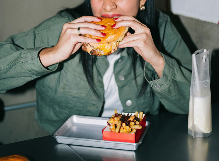Person eating a burger and fries at a table, highlighting diseases related to unhealthy eating habits from doctors' insights.
