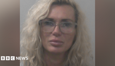 Kasha Sanderson has wavy blonde hair and is wearing glasses and makeup in a police mugshot.