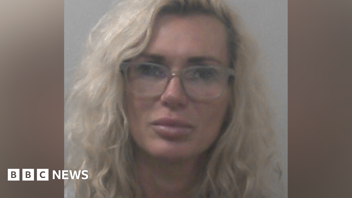 Kasha Sanderson has wavy blonde hair and is wearing glasses and makeup in a police mugshot.