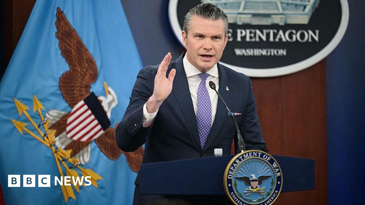 A satellite view of the Strait of Hormuz, with a thin stream of dark blue water flowing around a sharp point of arid land jutting into it.