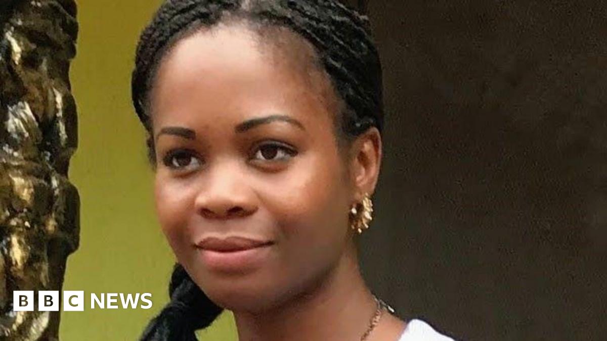 Frances has black braided hair and brown eyes. She is smiling and looking into the distance. She wears gold earrings and a gold necklace.