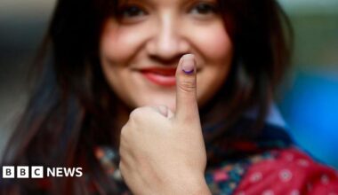 A female voter with long dark hair and wearing a red patterned dress shows her inked thumb after casting her ballot at a polling station during Nepal's parliamentary election in Kathmandu on March 5, 2026