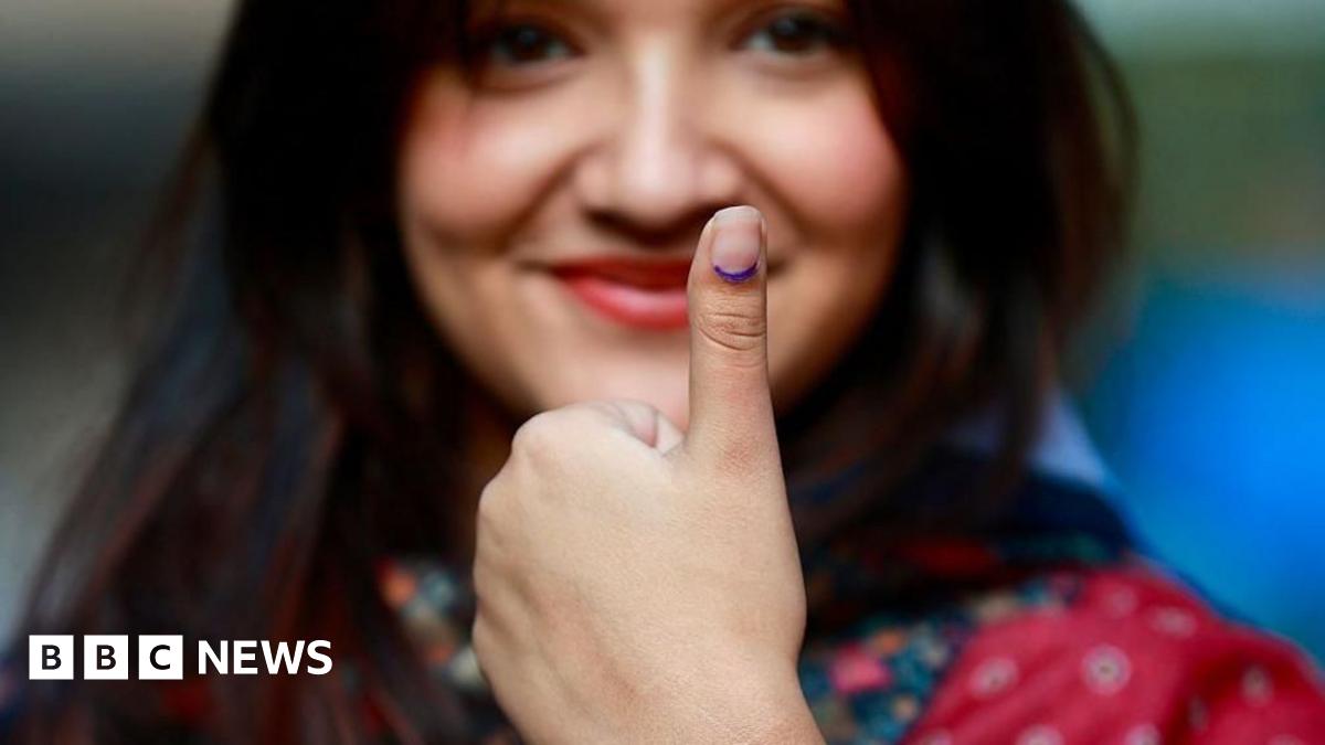 A female voter with long dark hair and wearing a red patterned dress shows her inked thumb after casting her ballot at a polling station during Nepal's parliamentary election in Kathmandu on March 5, 2026
